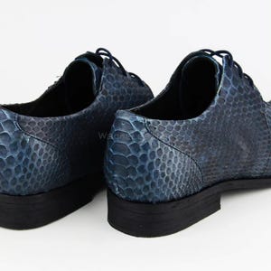 May include: A pair of blue leather dress shoes with a snakeskin pattern. The shoes have a lace-up design and a black sole. The shoes are displayed on a white background.