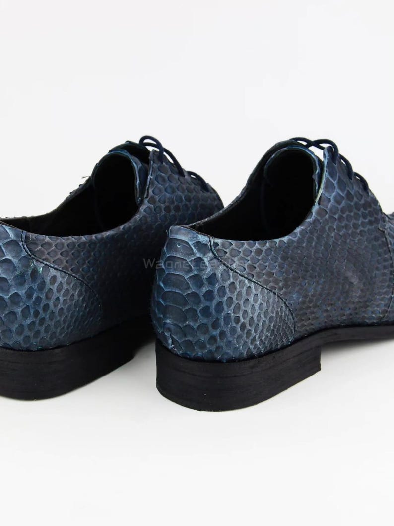 May include: A pair of blue leather dress shoes with a snakeskin pattern. The shoes have a lace-up design and a black sole. The shoes are displayed on a white background.