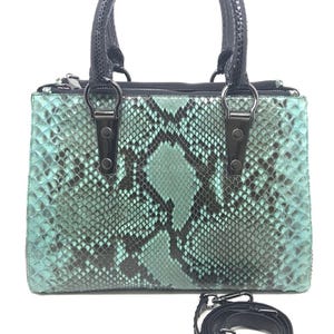 Może przedstawiać: Turkusowo-czarna torebka z wzorem skóry węża, z górnym uchwytem i odpinanym paskiem na ramię. Torba ma prostokątny kształt z zapięciem na zamek błyskawiczny i srebrnymi elementami. Uchwyty i pasek są czarne.