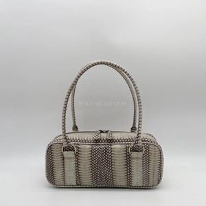 Puede incluir: Un bolso de mano gris claro con forma rectangular y dos asas redondeadas. El bolso presenta un estampado de piel de reptil en tonos grises y marrones. El texto "WaoneLeather" es visible en el bolso.