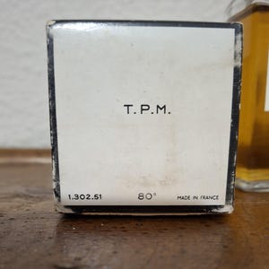 Pode incluir: Close-up de uma caixa de perfume vintage com o texto "T.P.M." em preto. Abaixo, os n&uacute;meros "1.302.51" e "80&deg;", com "MADE IN FRANCE" impresso na parte inferior. A caixa &eacute; branca com uma borda preta.