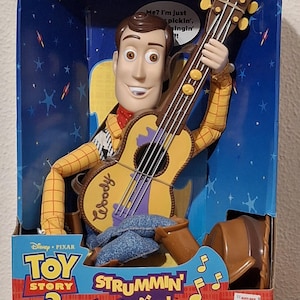 Puede incluir: Figura de "Woody que toca la guitarra y canta" de Toy Story 2 en su caja original. La mu&ntilde;eca Woody sostiene una guitarra. La caja tiene el logotipo de Disney Pixar y el texto "Me? I'm just pickin', singin'!"