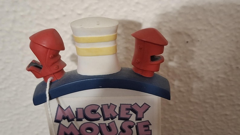 May include: A Mickey Mouse themed decorative item. The item features a white smokestack with yellow stripes, red accents, and the words "Mickey Mouse" in purple and white. The item has a blue base.