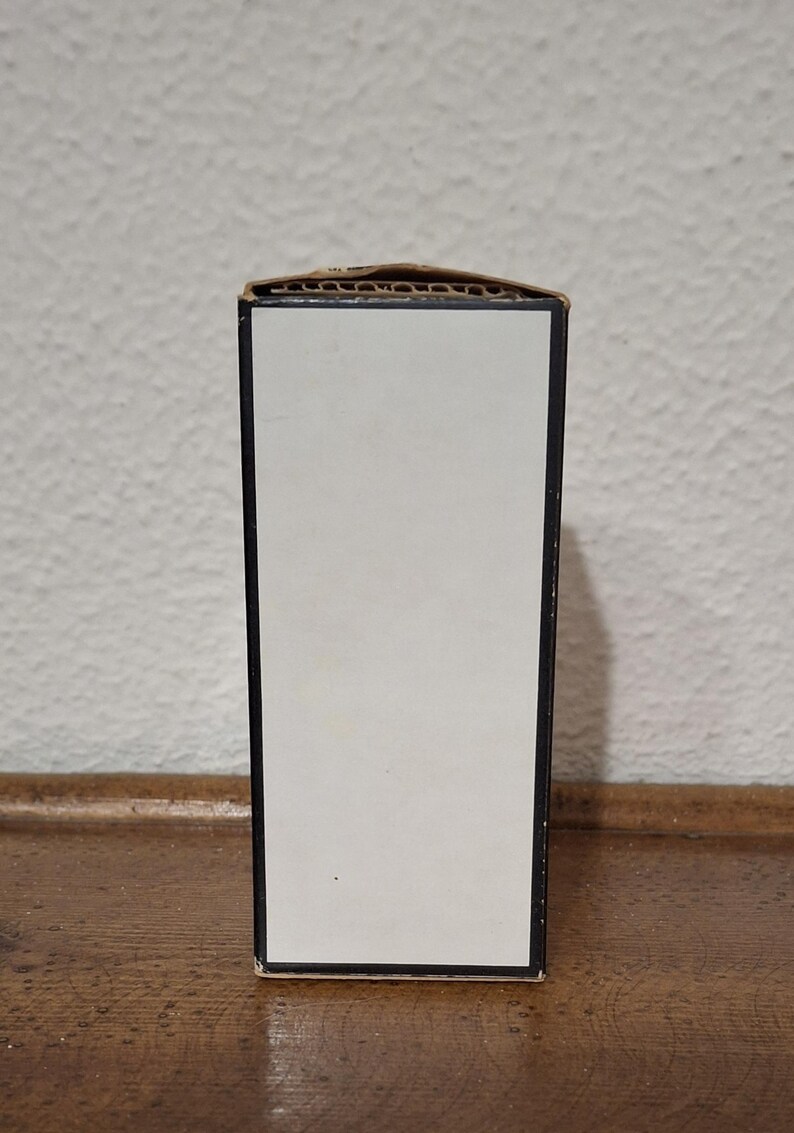 Pode incluir: Uma caixa retangular com um painel frontal branco e acabamento preto. A borda superior da caixa &eacute; feita de papel&atilde;o ondulado. A caixa est&aacute; colocada contra uma parede branca texturizada e uma superf&iacute;cie de madeira.