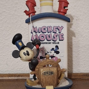 May include: A decorative figurine featuring Mickey Mouse as Steamboat Willie. The figurine has a white and blue boat with a wooden wheel and the text "1928". The text "Mickey Mouse Steamboat Willie" is also visible.