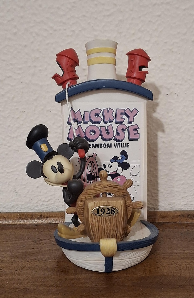 May include: A decorative figurine featuring Mickey Mouse as Steamboat Willie. The figurine has a white and blue boat with a wooden wheel and the text "1928". The text "Mickey Mouse Steamboat Willie" is also visible.