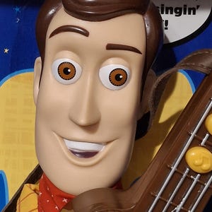 Puede incluir: Primer plano de una mu&ntilde;eca de Woody con cabello y ojos marrones, vistiendo una camisa amarilla con una bandana roja. La mu&ntilde;eca sostiene una guitarra marr&oacute;n. El texto de fondo dice: "&iquest;Yo? Solo estoy tocando, cantando!"