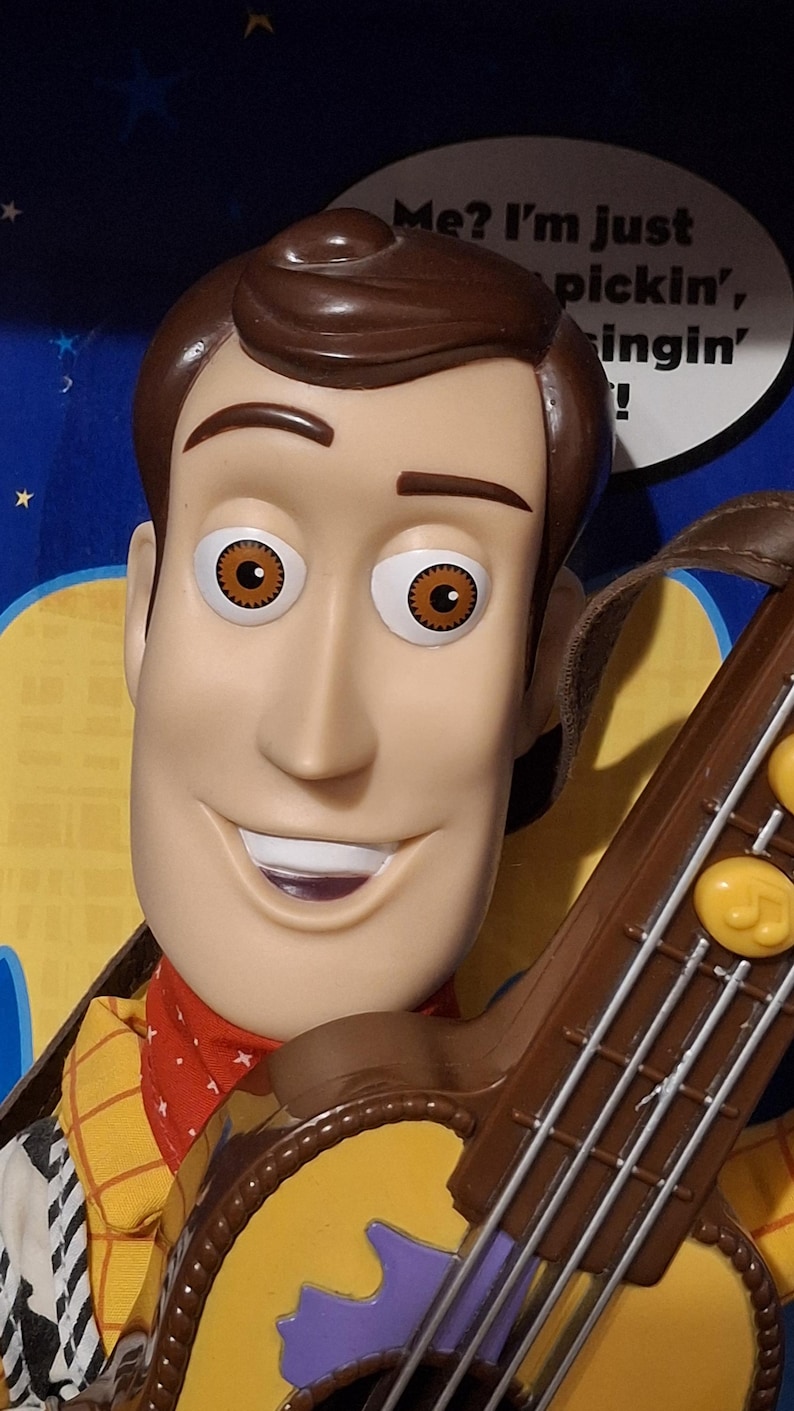 Puede incluir: Primer plano de una mu&ntilde;eca de Woody con cabello y ojos marrones, vistiendo una camisa amarilla con una bandana roja. La mu&ntilde;eca sostiene una guitarra marr&oacute;n. El texto de fondo dice: "&iquest;Yo? Solo estoy tocando, cantando!"