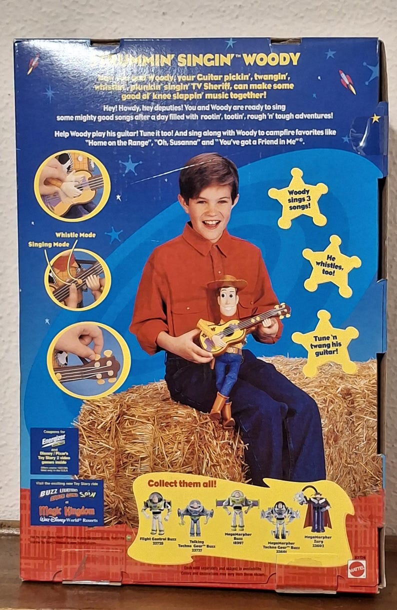 Puede incluir: Caja de la figura de Woody de Toy Story con una guitarra. El embalaje muestra a un ni&ntilde;o sosteniendo la mu&ntilde;eca de Woody, con el texto "Singin' Woody". La caja tambi&eacute;n muestra otros personajes de Toy Story.