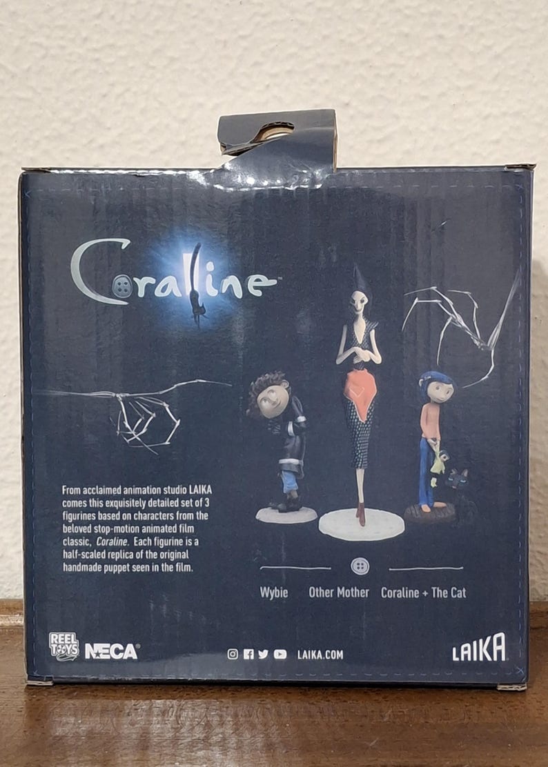 K&ouml;nnte beinhalten: Eine Box mit drei Coraline-Figuren. Die Box ist dunkelblau mit dem Titel "Coraline" in einer stilisierten Schriftart. Die Figuren umfassen Wybie, Other Mother und Coraline + The Cat.