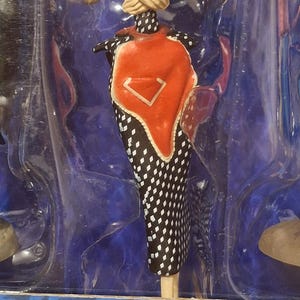 K&ouml;nnte beinhalten: Modepuppe in einer transparenten Kunststoffh&uuml;lle. Die Puppe tr&auml;gt ein schwarz-wei&szlig; gepunktetes Kleid mit einem roten und wei&szlig;en Akzent. Die Arme der Puppe sind verschr&auml;nkt, und sie hat ein einzigartiges, stilisiertes Design.