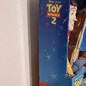 Puede incluir: Figura de acci&oacute;n de Woody de Toy Story 2 en su caja original. La caja azul presenta el logotipo de Disney Pixar Toy Story 2 y gr&aacute;ficos de estrellas. Woody lleva su atuendo de vaquero caracter&iacute;stico.