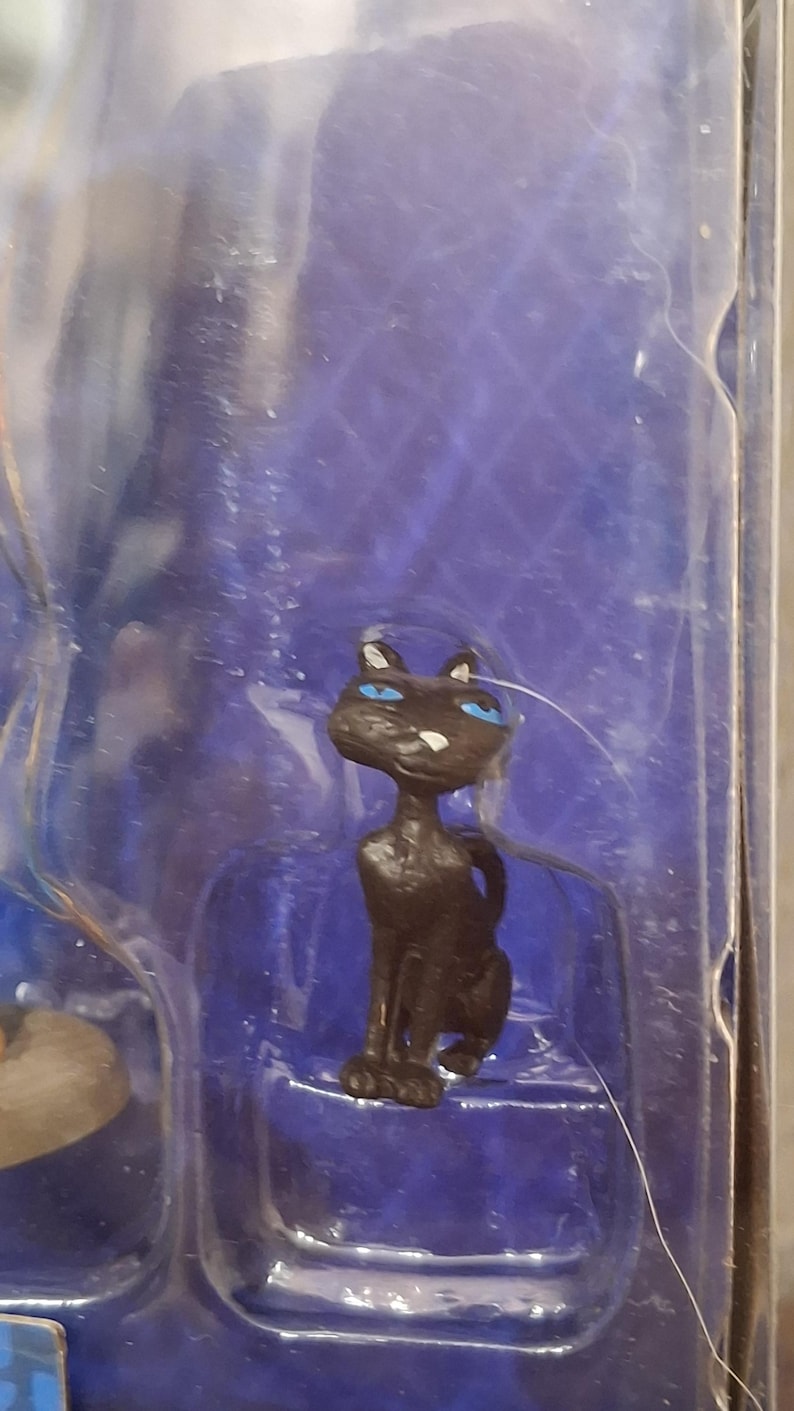 K&ouml;nnte beinhalten: Kleine, schwarze Katzenfigur mit leuchtend blauen Augen und wei&szlig;en Schnurrhaaren. Die Katze sitzt, der Schwanz ist eingerollt. Die Figur befindet sich in einer transparenten Kunststoffverpackung vor blauem Hintergrund.