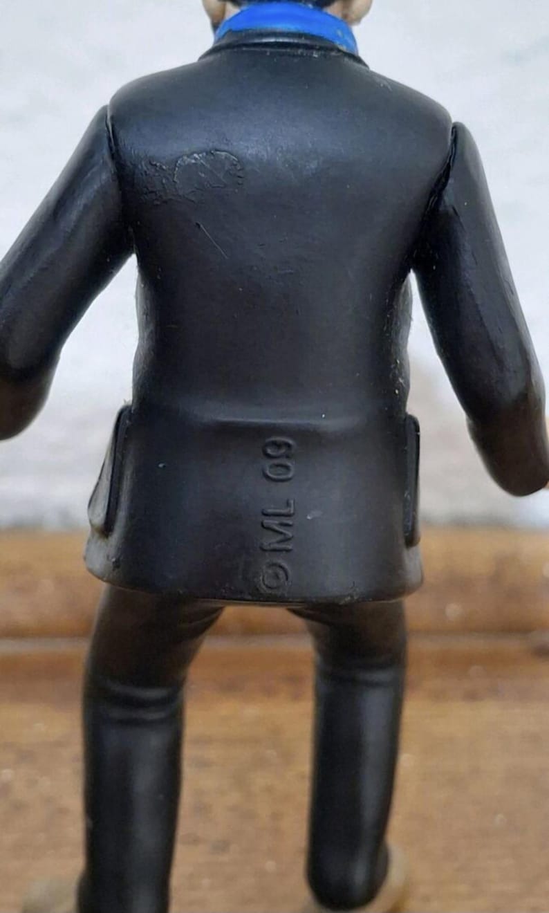 K&ouml;nnte beinhalten: Eine kleine Figur in einem schwarzen Sakko und passender Hose, von hinten betrachtet. Das Sakko hat ein blaues Kragendetail und tr&auml;gt den eingepr&auml;gten Text ML 09 im unteren R&uuml;ckenbereich. Die Figur hat eine glatte, matte Oberfl&auml;che.