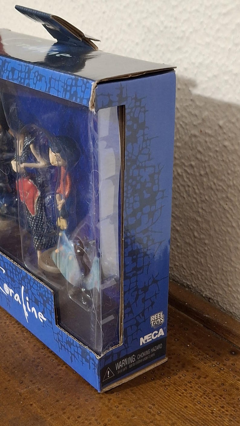 K&ouml;nnte beinhalten: Eine Actionfigur in einer blauen Box mit einem baumartigen Muster. Die Figur ist durch ein transparentes Fenster sichtbar. Die Box zeigt die Logos "NECA" und "Reel Toys".