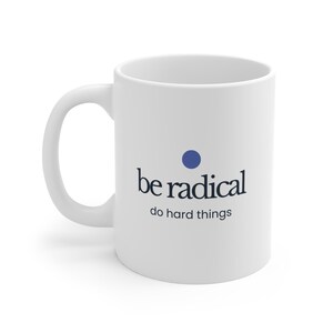 Pode incluir: Caneca de cerâmica branca com uma alça curva. A caneca apresenta o texto "be radical" em uma fonte estilizada, com um ponto azul acima do texto e as palavras "do hard things" abaixo.