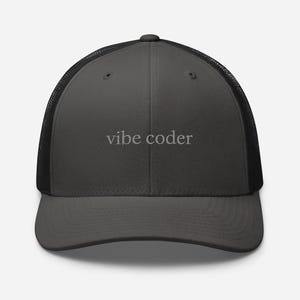 Puede incluir: Gorra de camionero gris carb&oacute;n con parte trasera de malla negra. El texto "vibe coder" est&aacute; bordado en gris claro en el panel frontal. La gorra tiene una visera curva y cierre a presi&oacute;n. Accesorio casual.