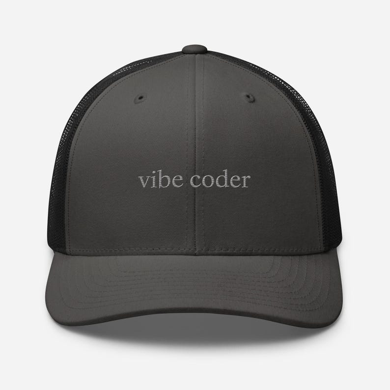 Puede incluir: Gorra de camionero gris carb&oacute;n con parte trasera de malla negra. El texto "vibe coder" est&aacute; bordado en gris claro en el panel frontal. La gorra tiene una visera curva y cierre a presi&oacute;n. Accesorio casual.