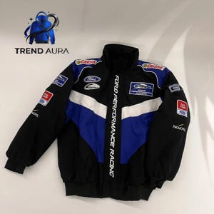 Op de afbeelding: Zwarte, blauwe en witte racejas met de tekst "FORD PERFORMANCE RACING". Voorzien van sponsorlogo's en een opstaande kraag. De jas heeft een sportief design.