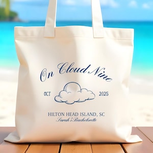 May include: Cream-colored tote bag with the text "On Cloud Nine" and a cloud illustration in navy blue. The bag also includes the date "OCT 2025" and the location "Hilton Head Island, SC".