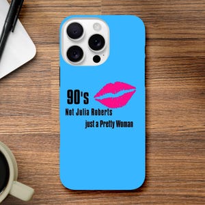 Könnte beinhalten: Hellblaue Handyhülle mit dem Text "90's Not Julia Roberts just a Pretty Woman" und einem pinkfarbenen Lippenabdruck. Die Hülle hat einen Kameraausschnitt und liegt auf einer Holzoberfläche.