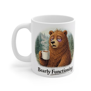 May include: White ceramic mug with a cartoon bear illustration. The bear, with a black eye, holds a coffee cup and looks tired. The mug has the text "Bearly Functioning" beneath the image of the bear.