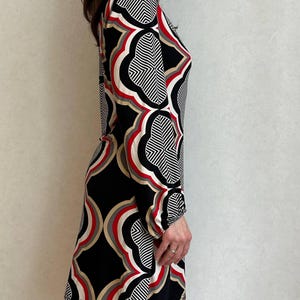 May include: A long-sleeved dress featuring a geometric pattern in black, white, red, and tan. The dress has a high neckline and a fitted silhouette, suitable for various occasions. The design incorporates repeating shapes and lines.