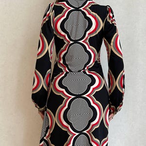 May include: A black dress with a geometric pattern in red, white, and tan. The long-sleeved dress has a high neckline and a fitted silhouette. The pattern is symmetrical and covers the entire dress.