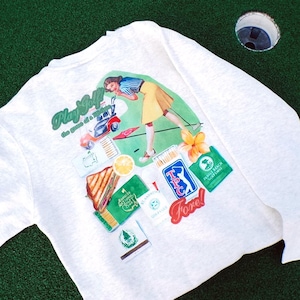 May include: White long-sleeve shirt with a golf-themed graphic. The graphic includes the text "Play Golf" and "Fore!" along with a vintage illustration of a woman golfing. Additional graphics include golf course logos and a sandwich.