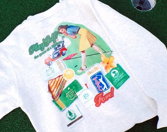 May include: White long-sleeve shirt with a golf-themed graphic. The graphic includes the text "Play Golf" and "Fore!" along with a vintage illustration of a woman golfing. Additional graphics include golf course logos and a sandwich.