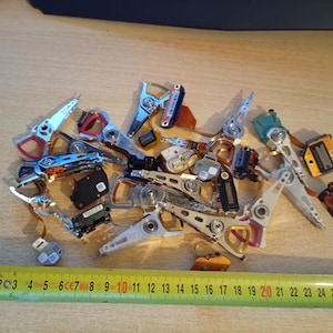 Peut inclure: Un ensemble de composants de disque dur d'ordinateur démontés, comprenant des têtes de lecture/écriture argentées et noires, des circuits imprimés et d'autres pièces internes. Un mètre ruban jaune avec des marquages noirs est au premier plan.