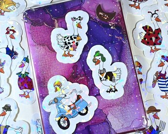 Może przedstawiać: Kolekcja fantazyjnych naklejek z gęsiami w różnych strojach, rozrzuconych wokół fioletowo-różowego etui na telefon. Naklejki przedstawiają gęsi przebrane za pirata, krowę i jadące na skuterze. Etui ma przezroczystą obwódkę.