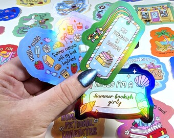 Może przedstawiać: Kolekcja holograficznych naklejek z letnimi i książkowymi wzorami. Jedna naklejka głosi "My summer is booked", inna "Hello I'm a summer bookish girly". Inne naklejki przedstawiają truskawki, książki i lody.