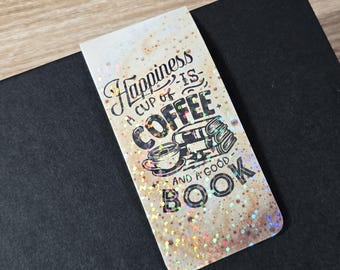 Może przedstawiać: Prostokątna zakładka do książki z napisem "Happiness is a cup of coffee and a good book". Zakładka ma błyszczący, nakrapiany wzór z ilustracjami filiżanki kawy i książek. Spoczywa na czarnej powierzchni.