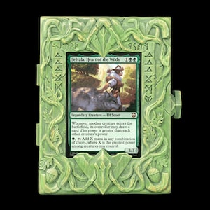 May include: A light green rectangular display frame featuring sculpted vine and acorn motifs, housing a Magic: The Gathering trading card titled Selvala, Heart of the Wilds. The frame has a textured, organic appearance with carved runic symbols.