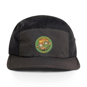 May include: Black five-panel cap with a curved brim. The cap features a circular patch with a cartoon bear wearing sunglasses, relaxing in a chair, and the words "CAMP VIBES ONLY". The bear is in front of a campfire and sunset.