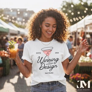 May include: A white t-shirt with a cocktail graphic and the words "Winning Design" in black script. The shirt also features the text "Just Mocks" and the initials "JM". The person in the image is holding a cocktail.