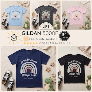 Könnte beinhalten: Ein Flatlay-Bundle von Kinder-T-Shirts in verschiedenen Farben, jedes mit einem Regenbogen-Design und dem Text "Your Winning Design Here". Das Bild enthält Turnschuhe, Stofftiere und dekorative Elemente. Der Text "GILDAN 5000B" und "34 FARBEN" sind ebenfalls sichtbar.