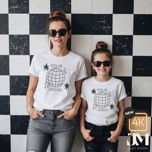 Könnte beinhalten: Zwei Personen tragen weiße T-Shirts mit einem Globus-Design und dem Text "YOUR DESIGN". Sie tragen Sonnenbrillen und stehen vor einer schwarz-weiß karierten Wand. Die Shirts sind im Rundhals-Stil.