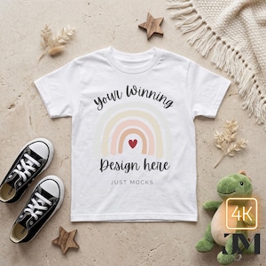 Könnte beinhalten: Weißes T-Shirt mit Regenbogen-Design und dem Text "your Winning Design here". Das Shirt wird mit schwarzen Turnschuhen, einem Plüschtier und Holzsternen auf einer neutralen Oberfläche präsentiert. Der Text "JUST MOCKS" ist ebenfalls sichtbar.