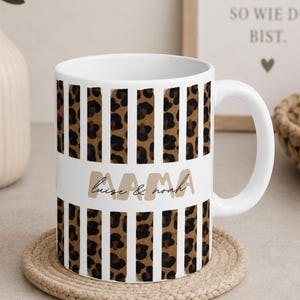 May include: A white ceramic mug featuring a repeating pattern of vertical leopard print stripes. A horizontal white band across the center displays the word MAMA in large beige letters with the names luise & noah written in black script below.