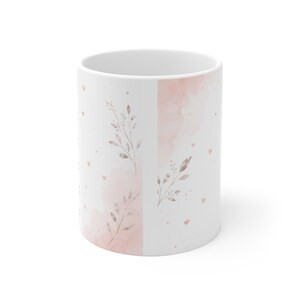 May include: A white ceramic mug featuring a delicate design of soft pink watercolor washes, small scattered hearts, and slender botanical sprigs with muted brown leaves. The pattern wraps around the exterior surface of the cylindrical vessel.