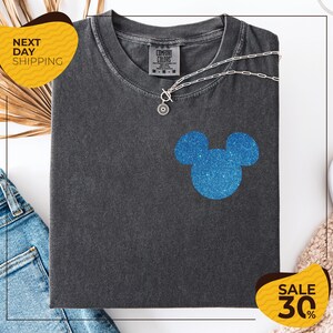 a gray t-shirt with a blue glittery Mickey Mouse design, along with a pair of blue jeans and a beige sweater. The t-shirt is displayed on a white background, and there are yellow and black sale signs indicating a 30% discount.