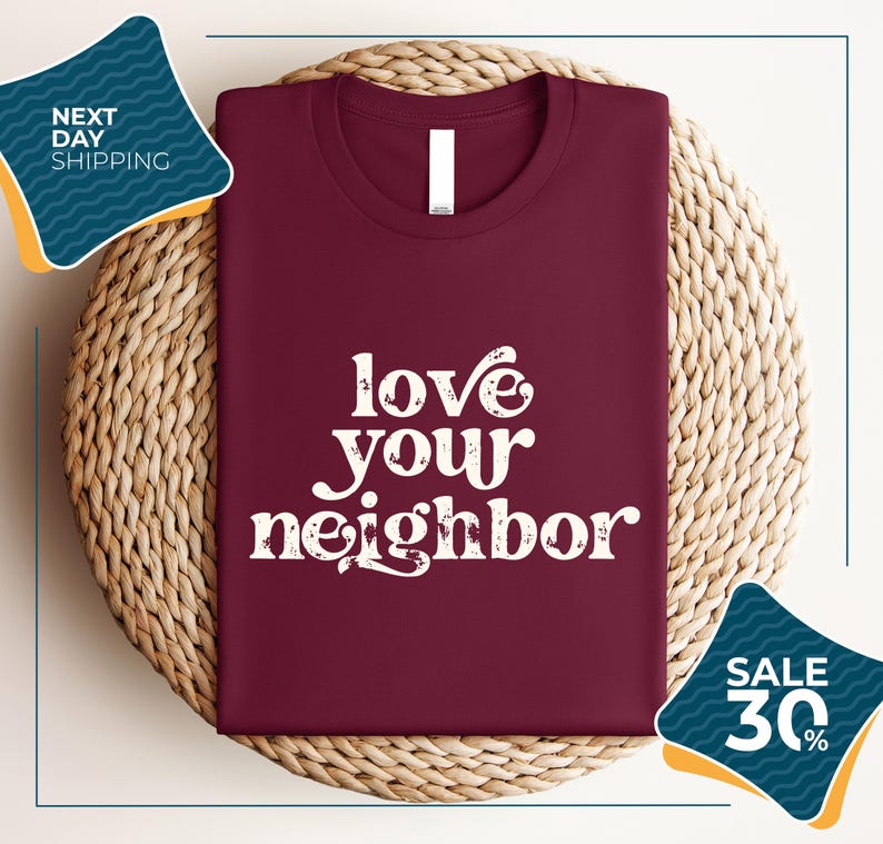 a burgundy t-shirt with the text "love your neighbor" printed on it, displayed on a woven placemat. The t-shirt is placed on a round wicker basket, and there are two sale signs in the image, one indicating a 30% discount and the other promoting next day shipping.