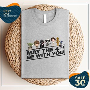 A gray t-shirt with a graphic design featuring characters from the Star Wars franchise, along with the text "May the 4th be with you".