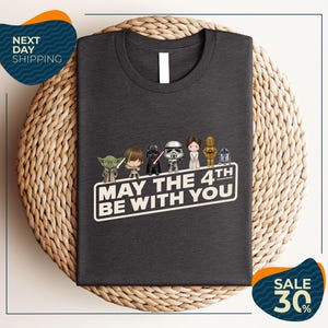 A gray t-shirt with a graphic design featuring characters from the Star Wars franchise, along with the text "May the 4th be with you".