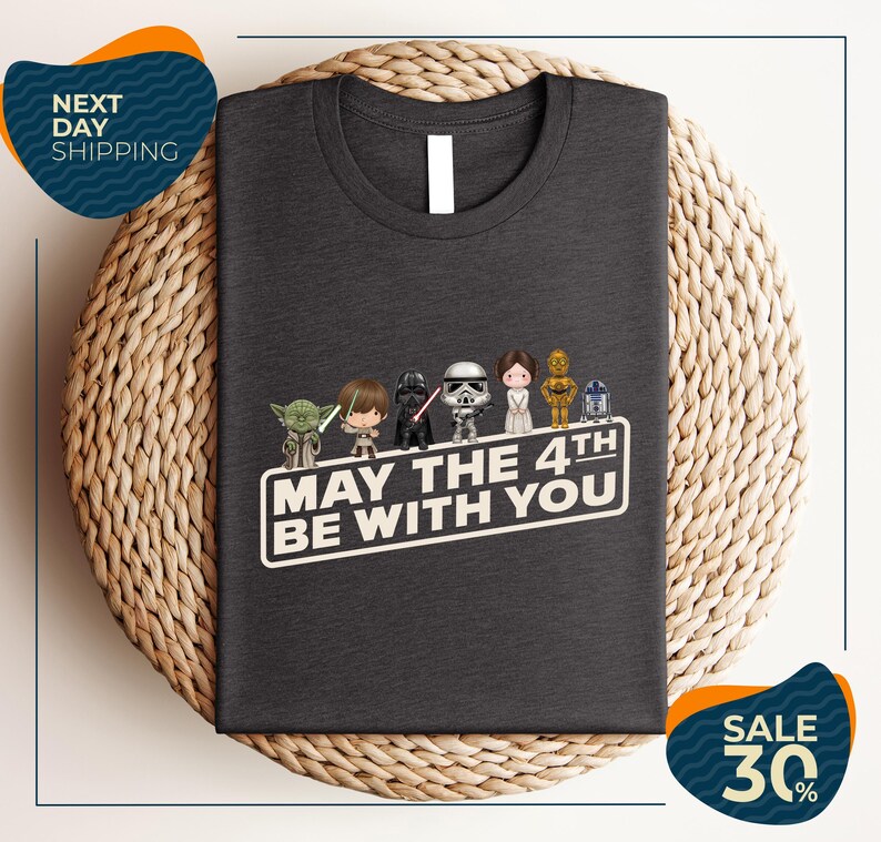A gray t-shirt with a graphic design featuring characters from the Star Wars franchise, along with the text "May the 4th be with you".