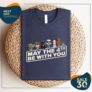 A navy blue t-shirt with a graphic design featuring characters from the Star Wars franchise, along with the text "May the 4th be with you".