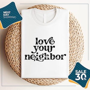 a white t-shirt with the text "LOVE YOUR NEIGHBOR" printed on it, displayed on a woven placemat. The t-shirt is placed on a round wicker basket, and there are two sale signs in the image, one indicating a 30% discount and the other promoting next day shipping.