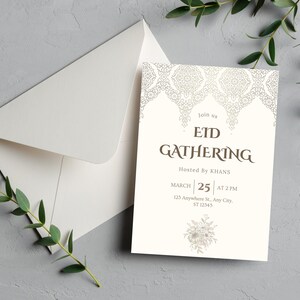 May include: An invitation card and envelope set for an Eid Gathering. The card is off-white with decorative patterns and text that reads "EID GATHERING" and event details. The envelope is white, and the background is a textured gray surface.
